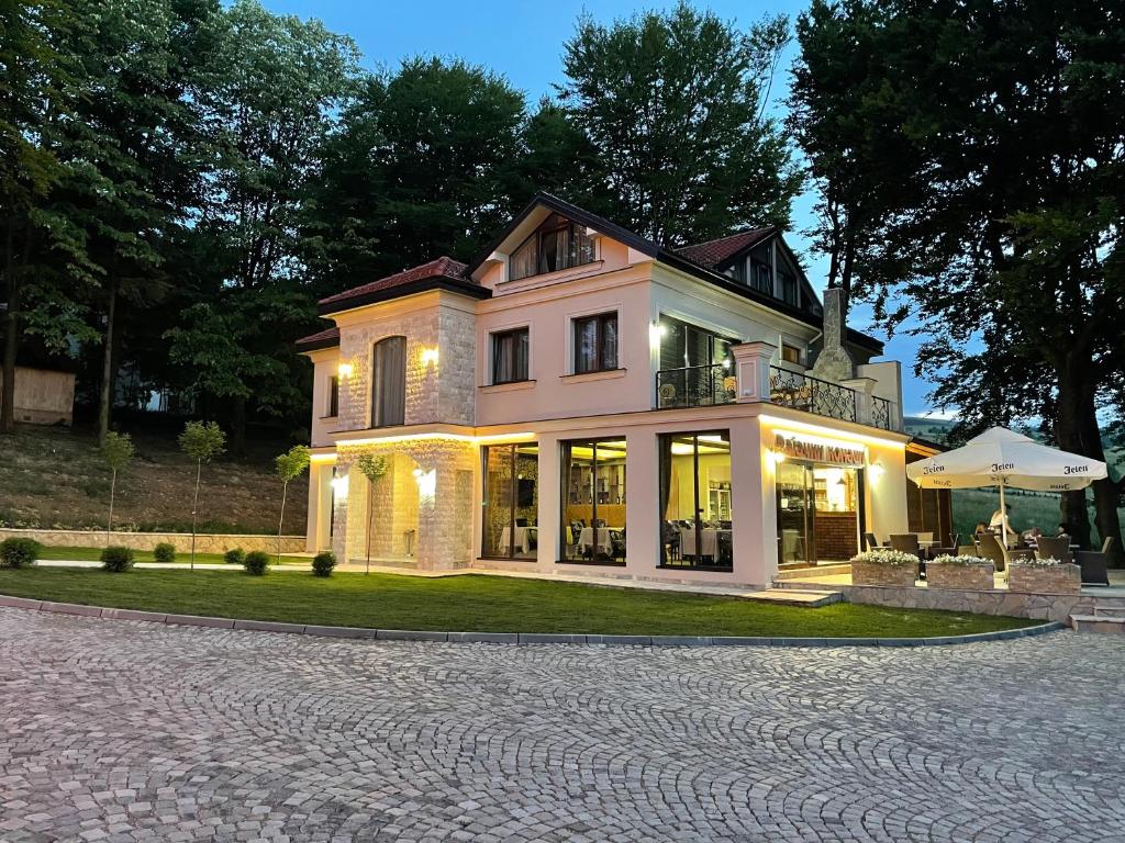 ein großes weißes Haus mit einer Terrasse auf einer Auffahrt in der Unterkunft Rajački Konaci in Polom