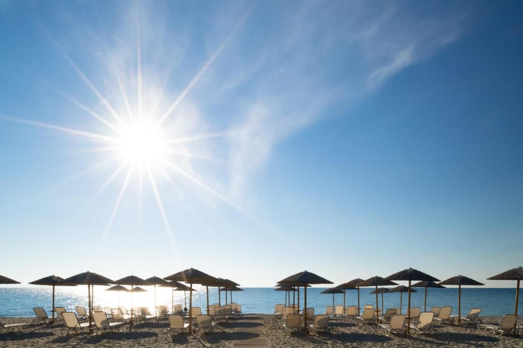 a beach with umbrellas and chairs and the sun at Olympios Zeus in Plaka Litochorou