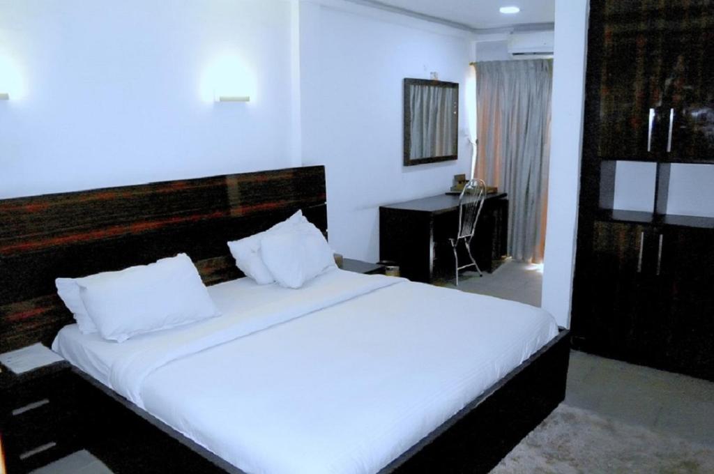 um quarto com uma cama grande com lençóis brancos e uma secretária em Park Hotels em Port Harcourt