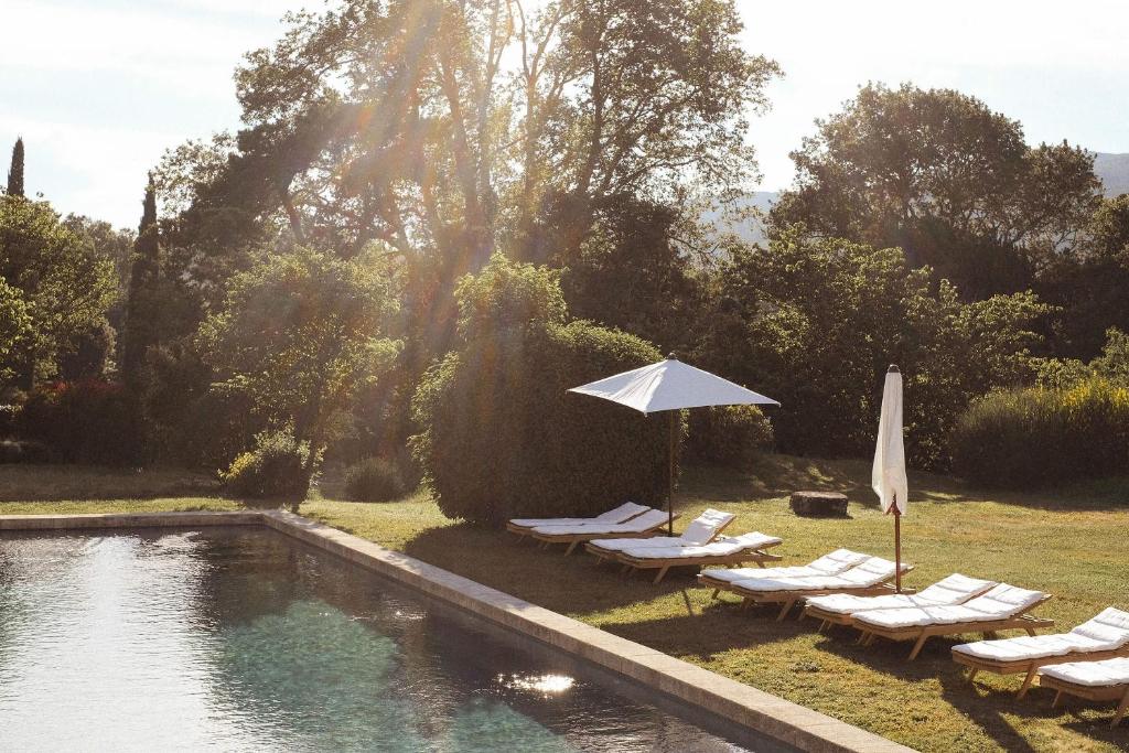 a swimming pool with lounge chairs and an umbrella and a swimming pool at Le Galinier, a Beaumier hotel in Lourmarin