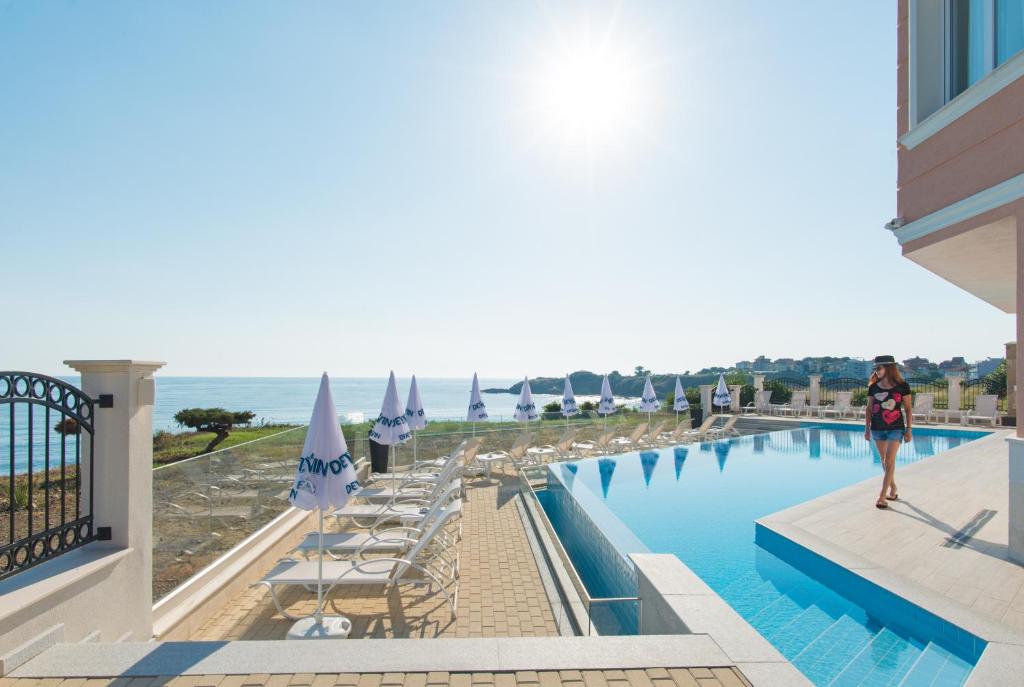 a woman walking by a swimming pool with the ocean in the background at CASA PARADISO Apartments in Ahtopol