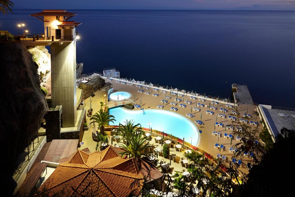 a view of a swimming pool and a beach at night at The Cliff Bay - PortoBay in Funchal