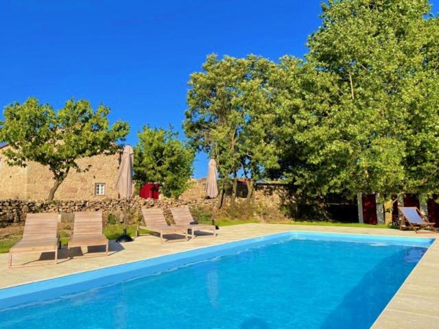 a swimming pool with chaises and chairs and trees at Quinta do Rio Noémi in Guarda