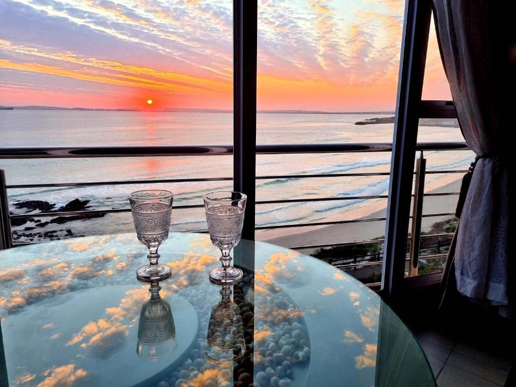 a table with two wine glasses on a table with a view of the ocean at Crystal Lagoon Lodge in Langebaan