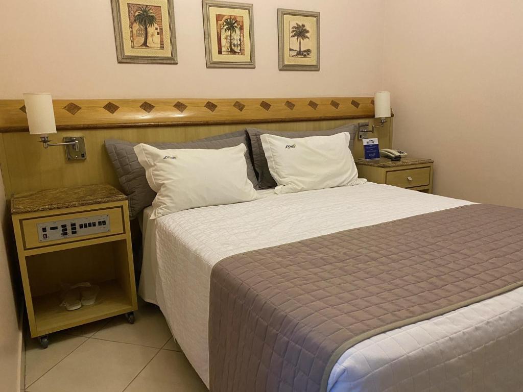 een slaapkamer met een groot bed met witte lakens en kussens bij L'Opera Hotel in Sao Paulo