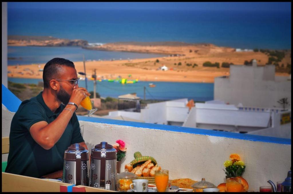 un hombre tomando una copa en una mesa con vistas a la playa en Dar Doukkala Oualidia, en Oualidia