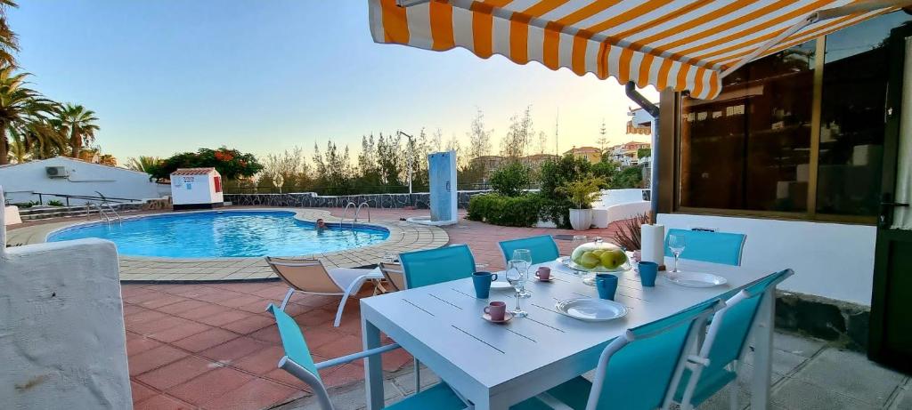 une table blanche avec des chaises bleues et une piscine dans l'établissement ARGUINEGUIN, two bedrooms bungalow, pool & wifi, à Arguineguín