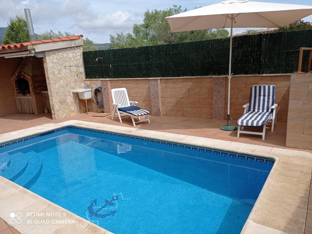 una piscina con 2 sillas y una sombrilla en Villa descanso, en Alcanar