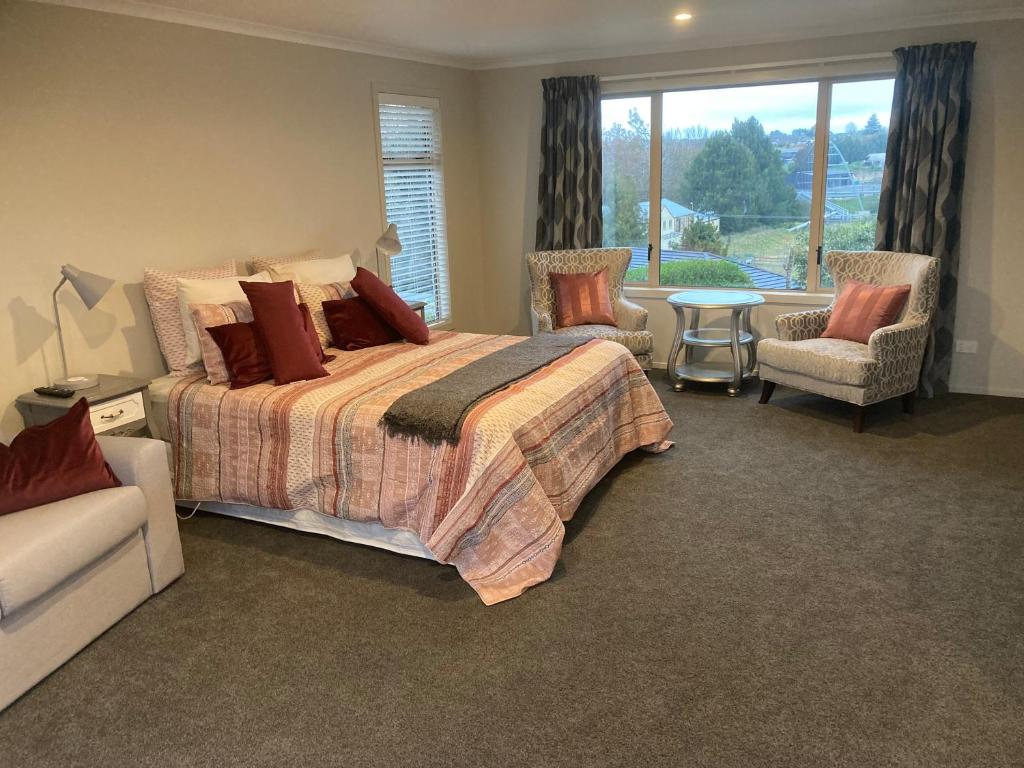 a bedroom with a bed and chairs and a window at Cambridge Te Awa Rivertrail BnB in Cambridge