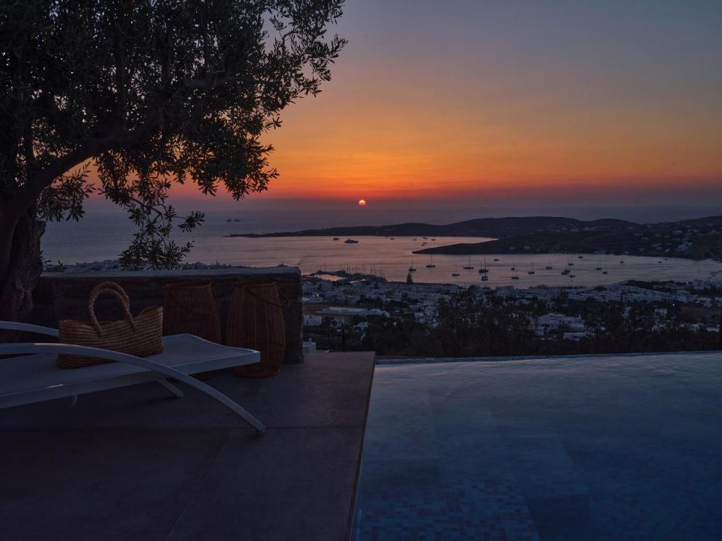 a sunset from a patio with a bench and a table at Infinity sea view cosy villa with private pool in Parikia