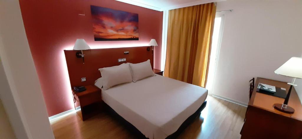 a bedroom with a white bed and a red wall at Hotel Cabañas in Puertollano