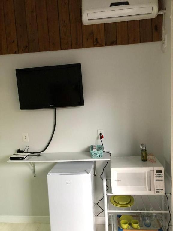 a television on a wall above a microwave at SUITE RUA PESCADA AMARELA in Bombinhas
