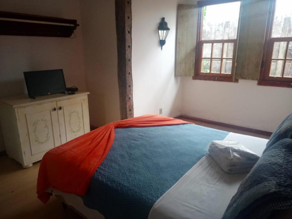 a bedroom with a bed with an orange blanket on it at Chalé das Flores in Tiradentes