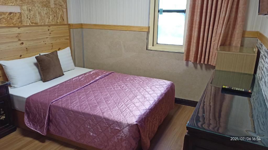 a bedroom with a bed with a purple comforter and a window at 鑽石大旅社 in Pingtung City