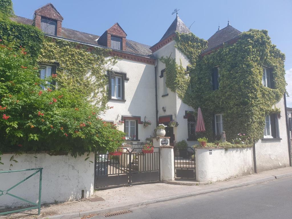 uma casa branca com um portão preto e arbustos em Sunset House Chambres de Hotes em Magnac-Laval