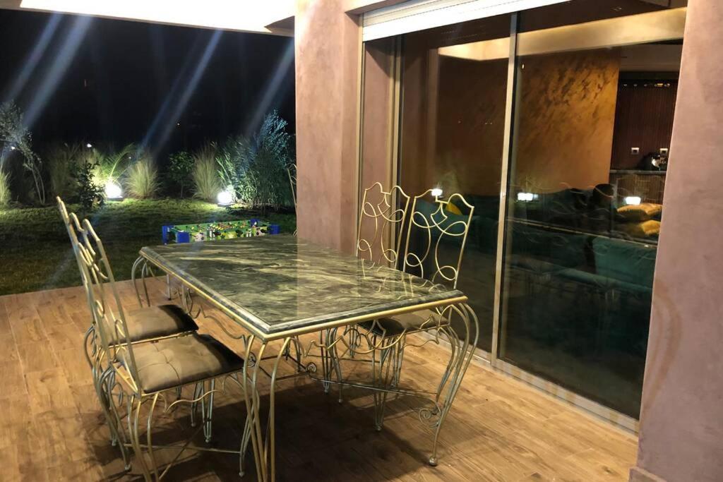 een glazen tafel en stoelen op een patio bij Cosy Loft Emeraude Marrakech Prestigia Golf City in Marrakesh