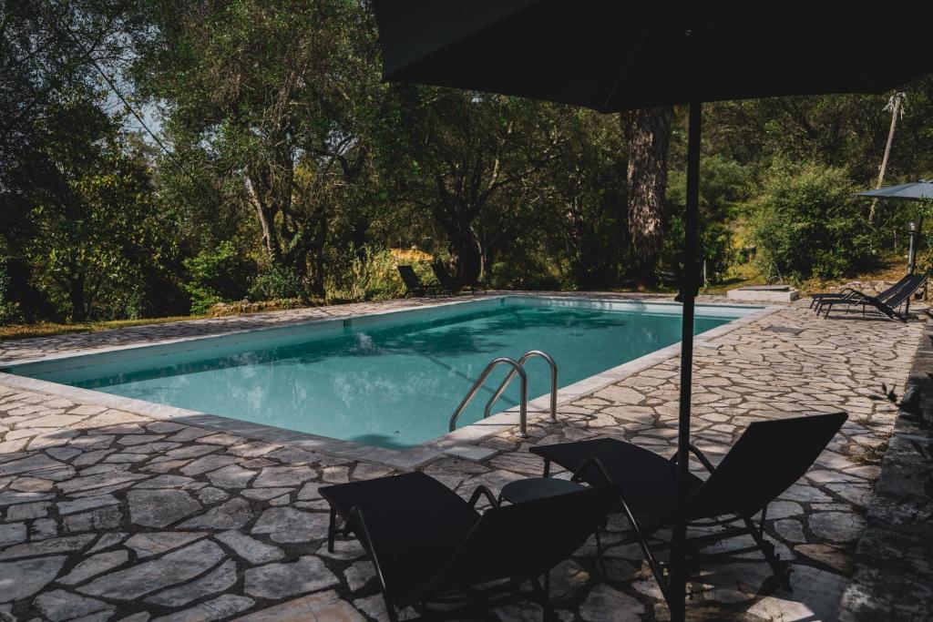 a swimming pool with two chairs and an umbrella at Dimoulitsa Villas Complex in Doukádes