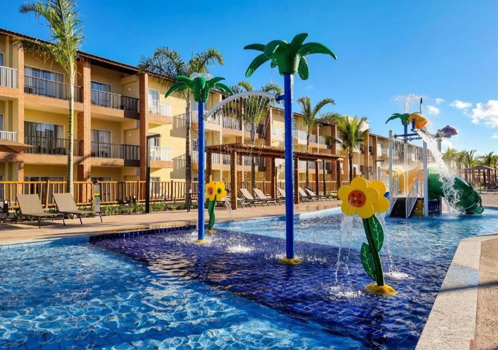 una piscina en un complejo con palmeras y una fuente en Apartamento Ondas Resort en Porto Seguro