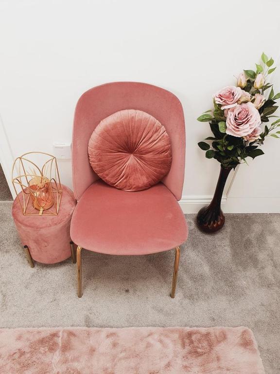 einen rosa Stuhl neben einer Vase mit Blumen in der Unterkunft Deluxe Spacious Apartment in Chadwell Heath, London in Goodmayes