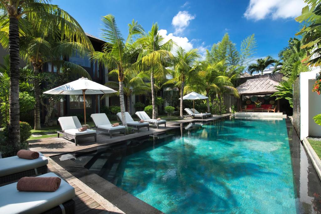 una piscina en un complejo con sillas y sombrillas en Villa Abakoi, en Seminyak