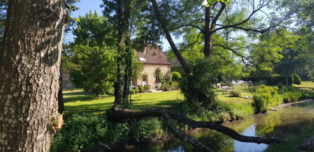 La maison d'amis du moulin في La Chapelle-Viel: منزل في حديقة بها نهر وأشجار