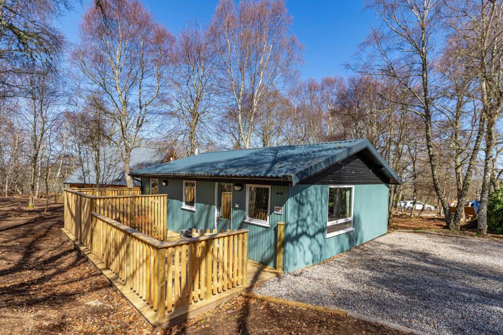 uma pequena casa verde com uma cerca de madeira em Heather Lodge 12 with Hot Tub em Belladrum