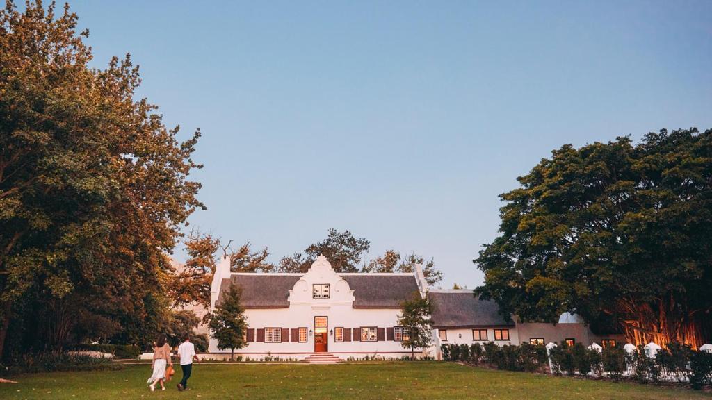 eine Gruppe von Menschen, die vor einem weißen Haus spazieren in der Unterkunft Blaauwklippen Manor by NEWMARK in Stellenbosch