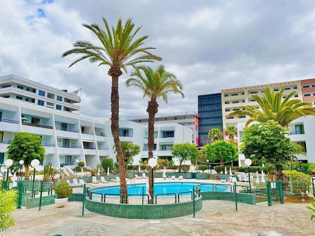 a swimming pool with palm trees in front of a building at Optimist Playa de Las Américas in Playa de las Americas