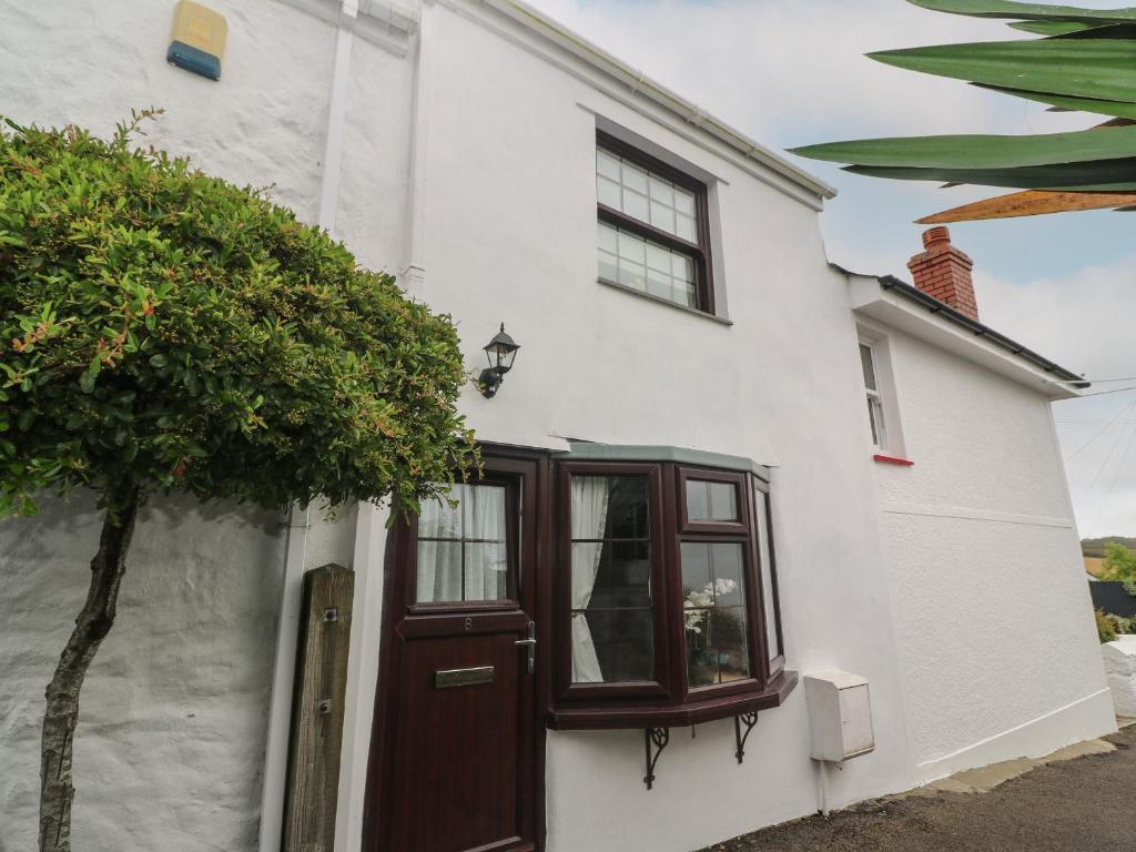 a white house with a brown door and a tree at Primrose Cottage in Hayle