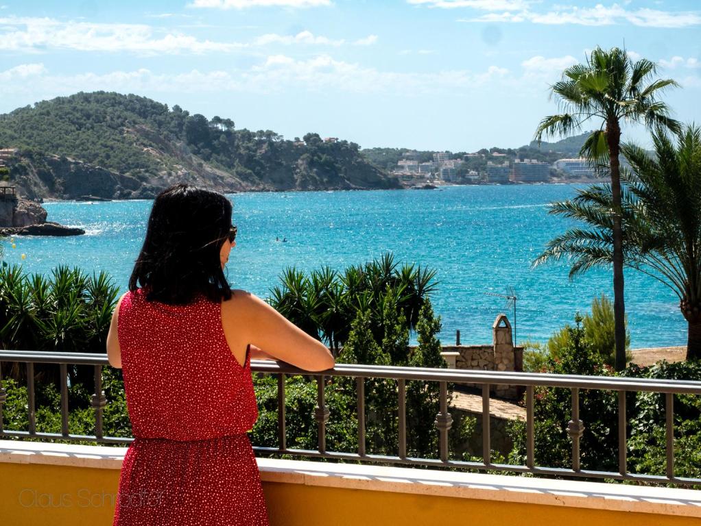 Una mujer con un vestido rojo mirando hacia el océano en Hotel Flor Los Almendros, en Paguera