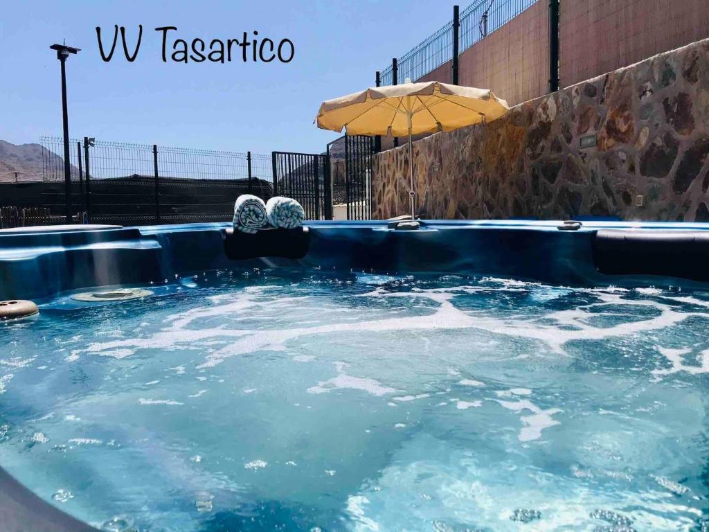 - un bain à remous avec de l'eau bleue et un parasol dans l'établissement Vv Tasartico with hot tub, à Tasartico