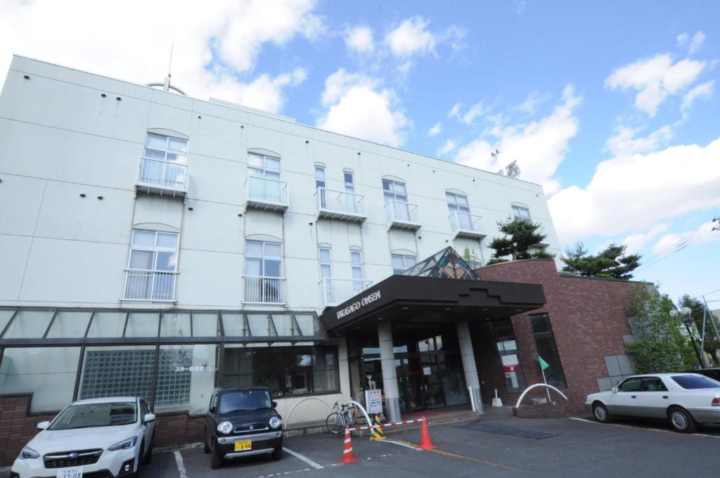 a white building with cars parked in a parking lot at Takasago Onsen in Asahikawa