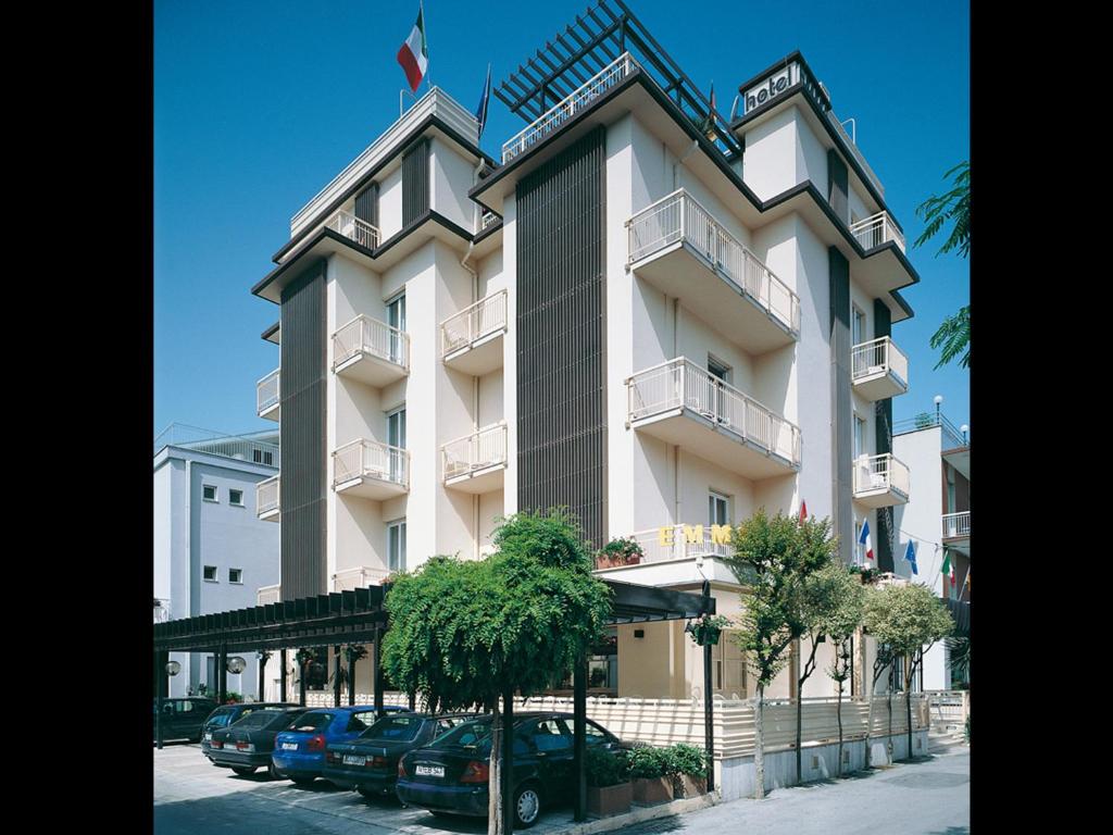 un grande edificio bianco con macchine parcheggiate di fronte di Hotel Emma Nord a Rimini