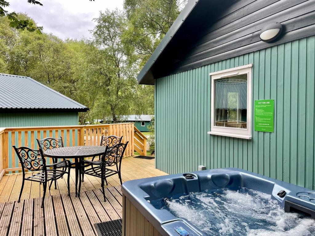 a hot tub on a deck with a table and chairs at Bracken Lodge 8 with Hot Tub in Belladrum