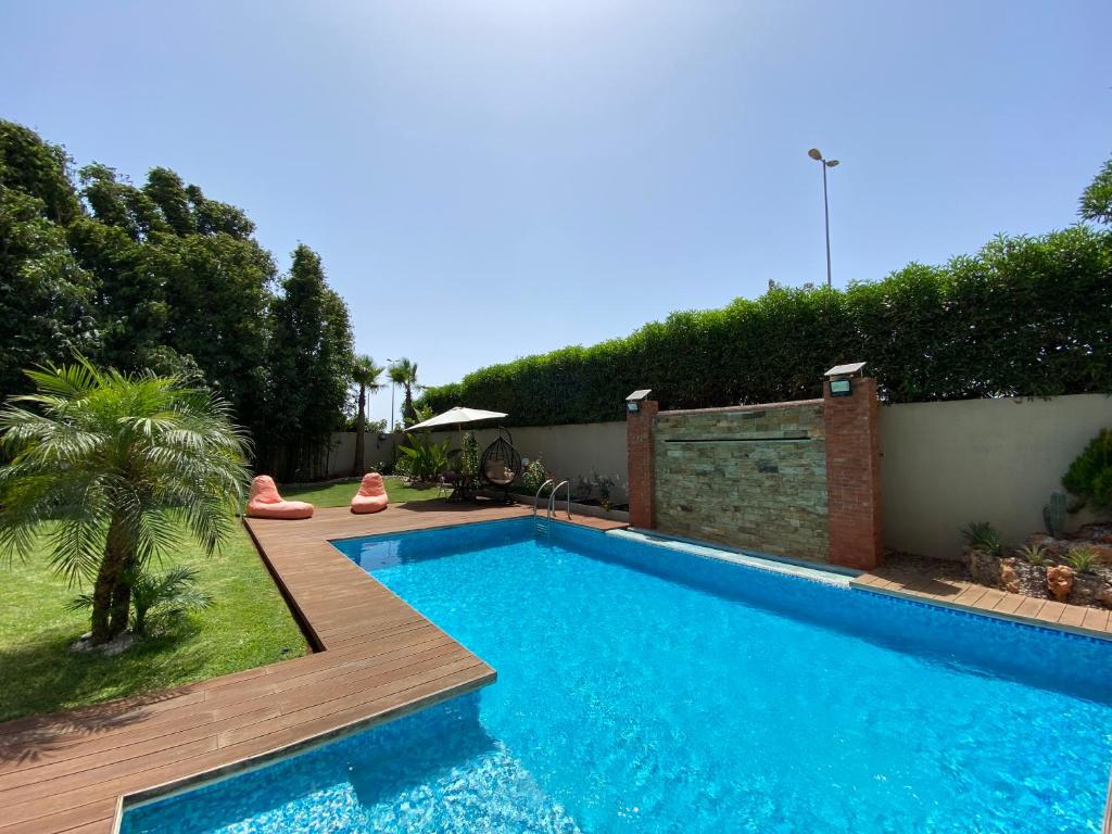 a swimming pool with a wooden deck next to a yard at Lilas Park Villa - Casablanca Bouskoura in Casablanca