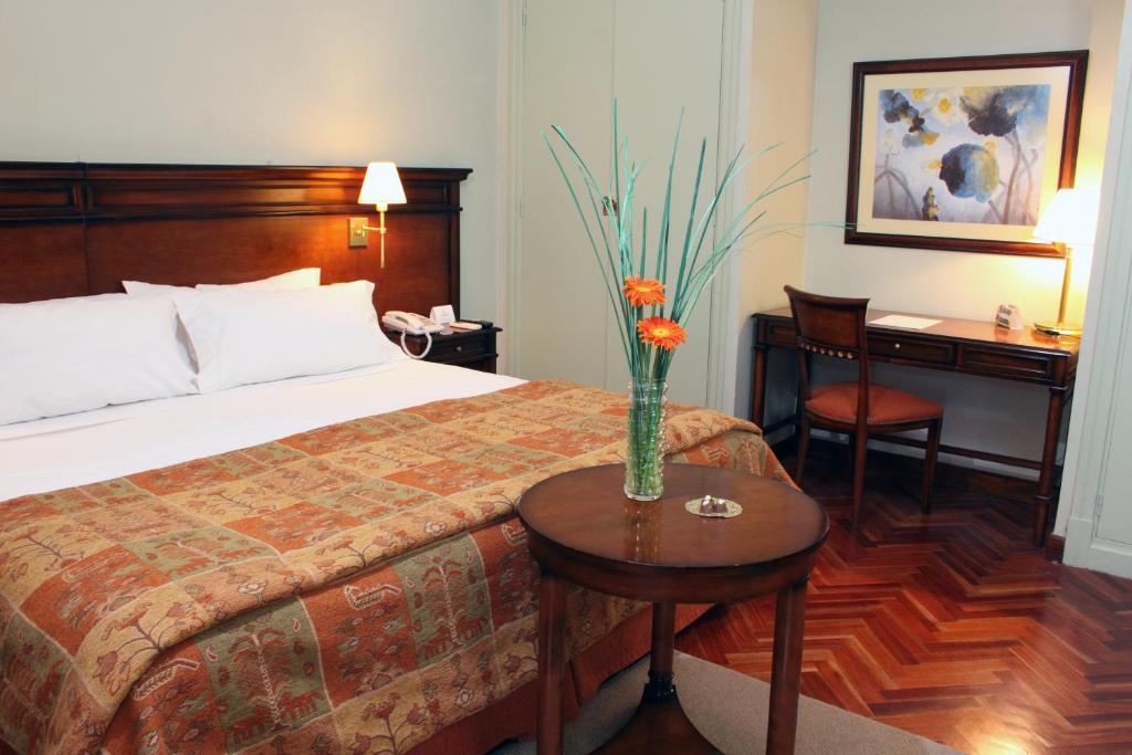 a hotel room with a bed and a table with a vase on it at Hotel Colonial San Nicolás in San Nicolás de los Arroyos