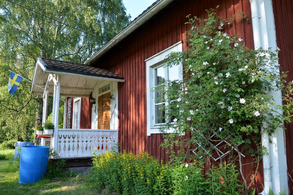 a red house with a white porch and a tree at Lillstugan, södra Bergslagen in Surahammar