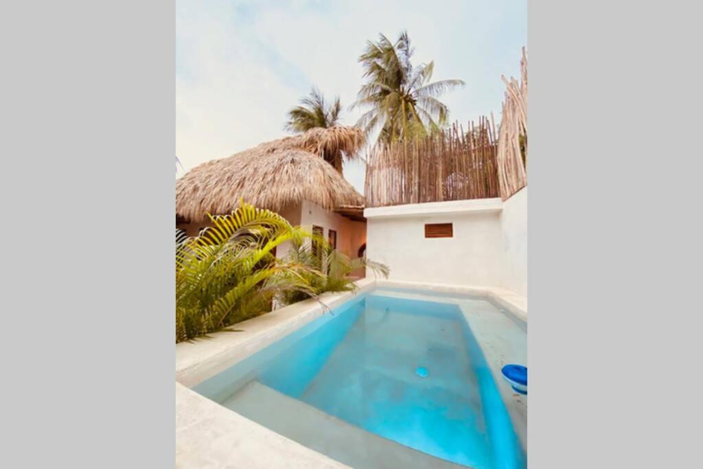 a swimming pool next to a house with a thatch roof at Casa Coconut in Puerto Escondido