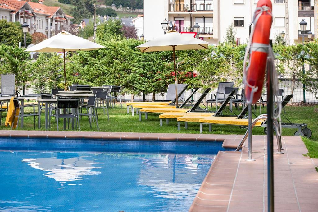 uma piscina com cadeiras, mesas e guarda-sóis em Parador de Limpias em Limpias