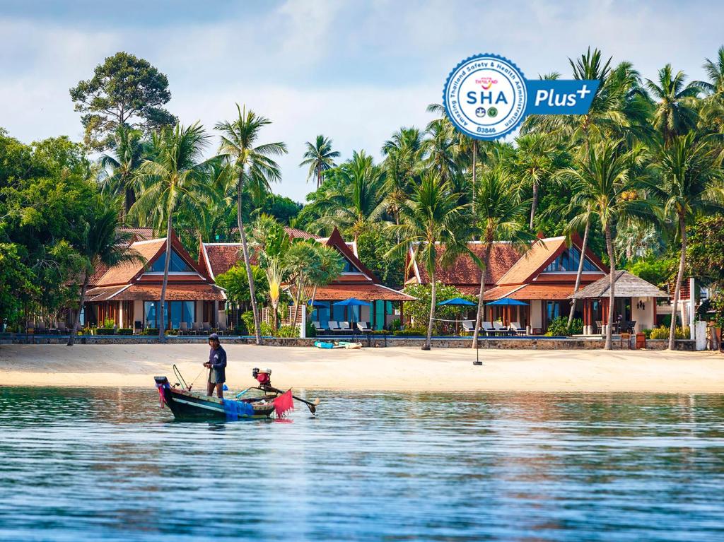 a man standing on a boat in the water near a beach at Tawantok Beach Villas - SHA Extra Plus in Lipa Noi