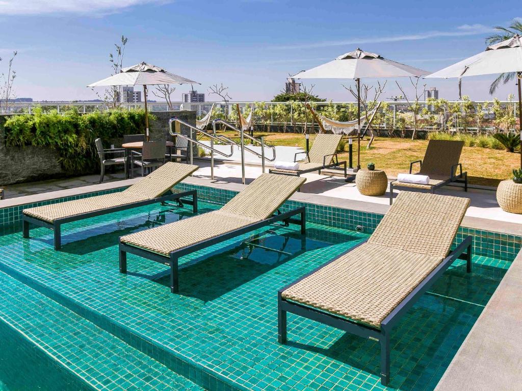 einen Pool mit Stühlen und Sonnenschirmen in einem Resort in der Unterkunft Novotel Lencois Paulista in Lençóis Paulista