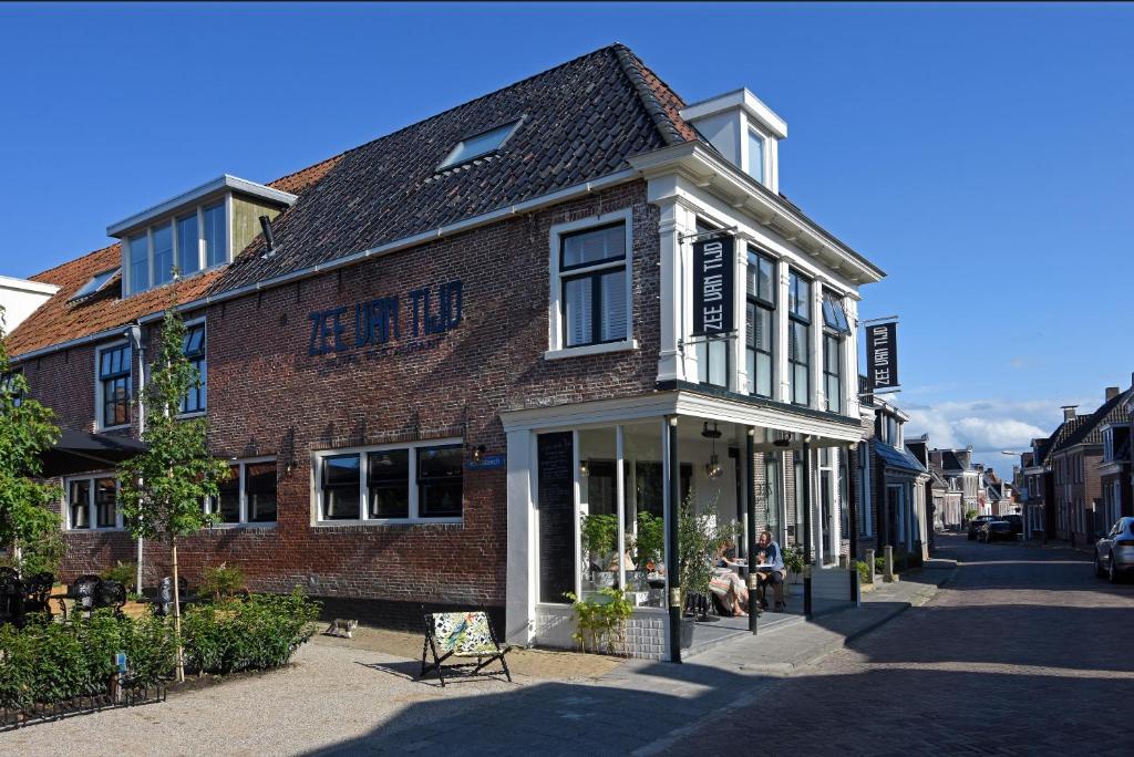 un edificio de ladrillo en una calle con gente sentada afuera en Zee van Tijd Holwerd en Holwerd
