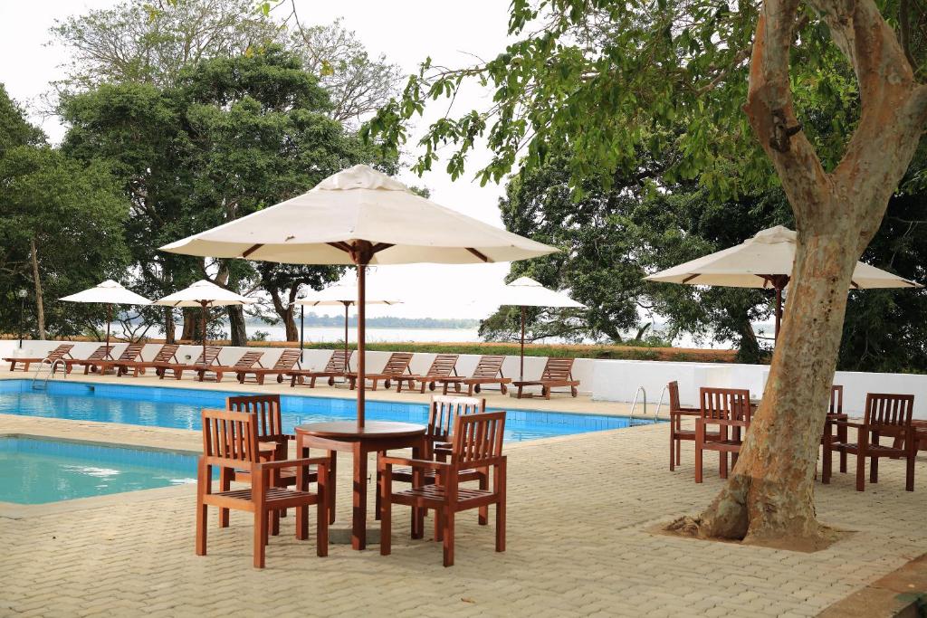 einen Tisch und Stühle mit Sonnenschirmen neben einem Pool in der Unterkunft The Lakeside at Nuwarawewa in Anuradhapura