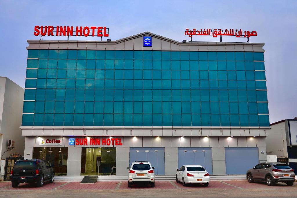 a building with cars parked in a parking lot at Sur Inn Hotel Apartments صور ان للشقق الفندقية in Sur