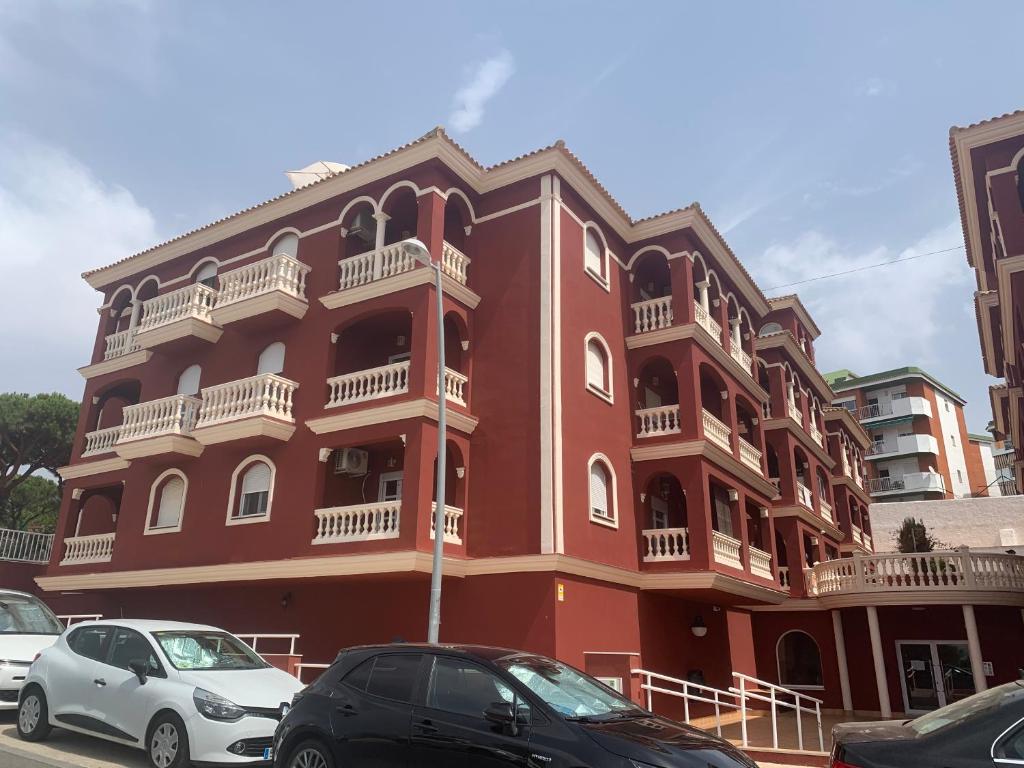 a red building with cars parked in front of it at Apartamento PUERTO in Mazagón