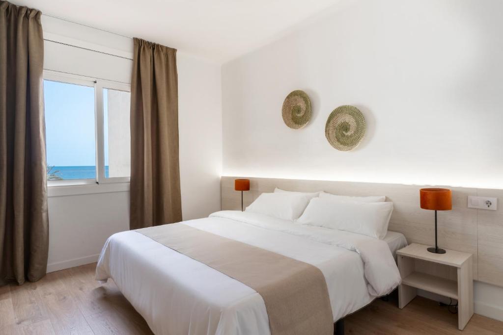a white bedroom with a large bed and a window at Apartamentos Venecia in Lloret de Mar