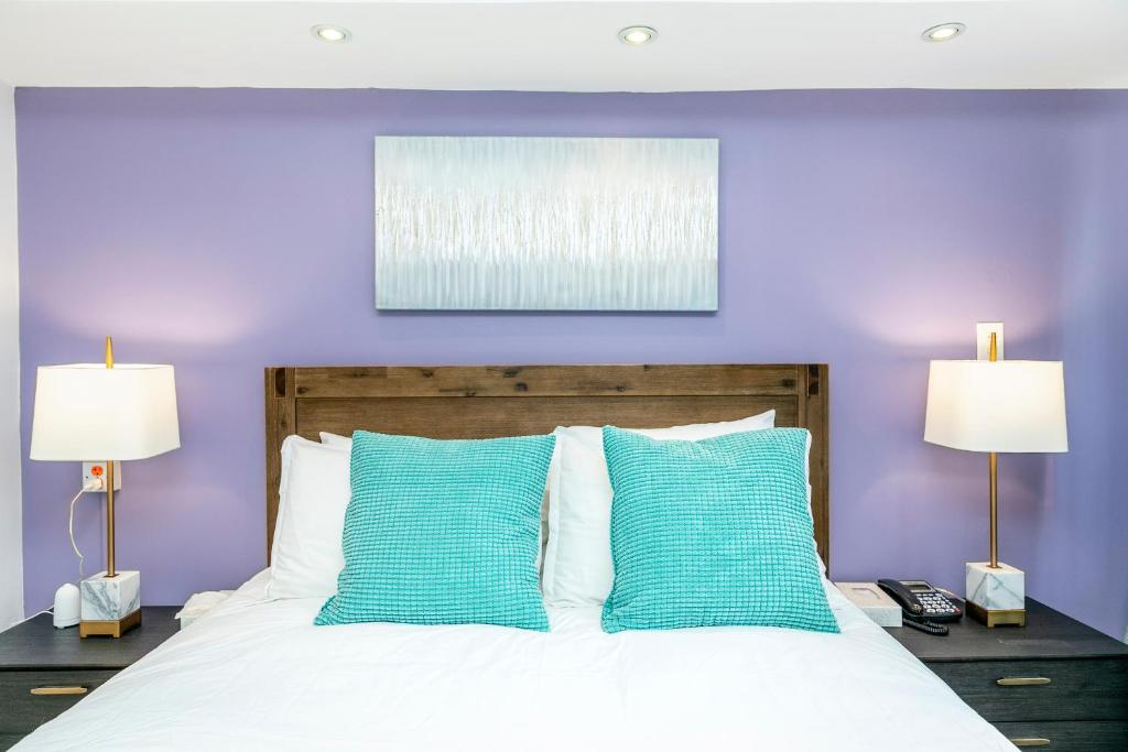 Motel Rideau في بروسارد: غرفة نوم أرجوانية مع سرير أبيض مع وسائد زرقاء