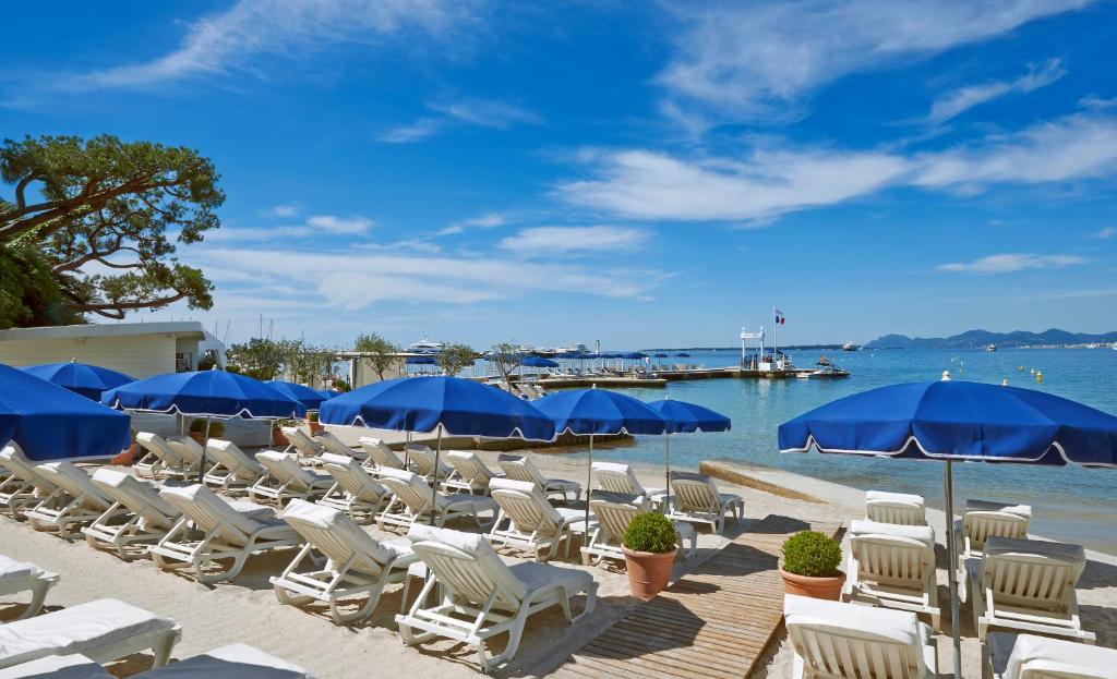 a bunch of chairs and blue umbrellas on a beach at Hôtel Belles Rives in Juan-les-Pins