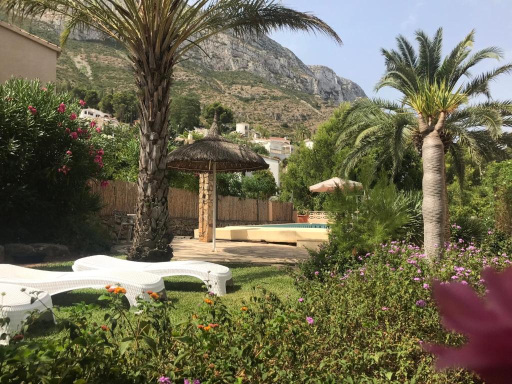 een tuin met twee witte stoelen en palmbomen en een berg bij Villa Marta - Montgó in Denia