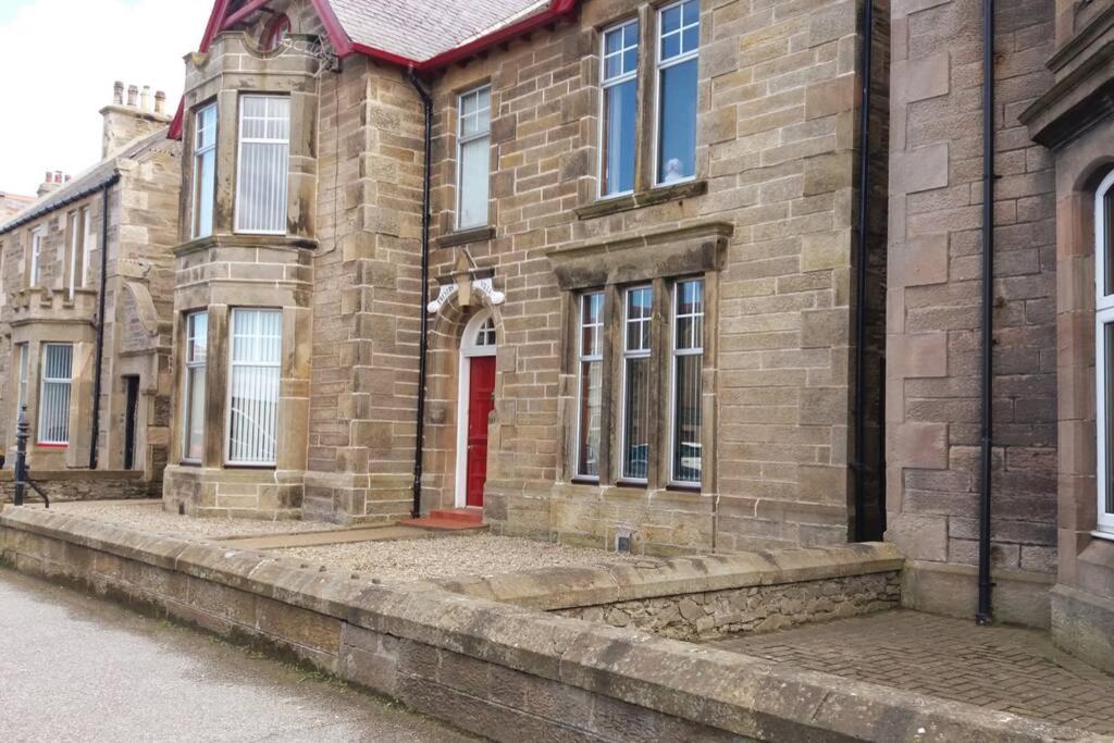 a brick building with a red door on a street at Preston Villa, spacious ground floor apartment in Buckie